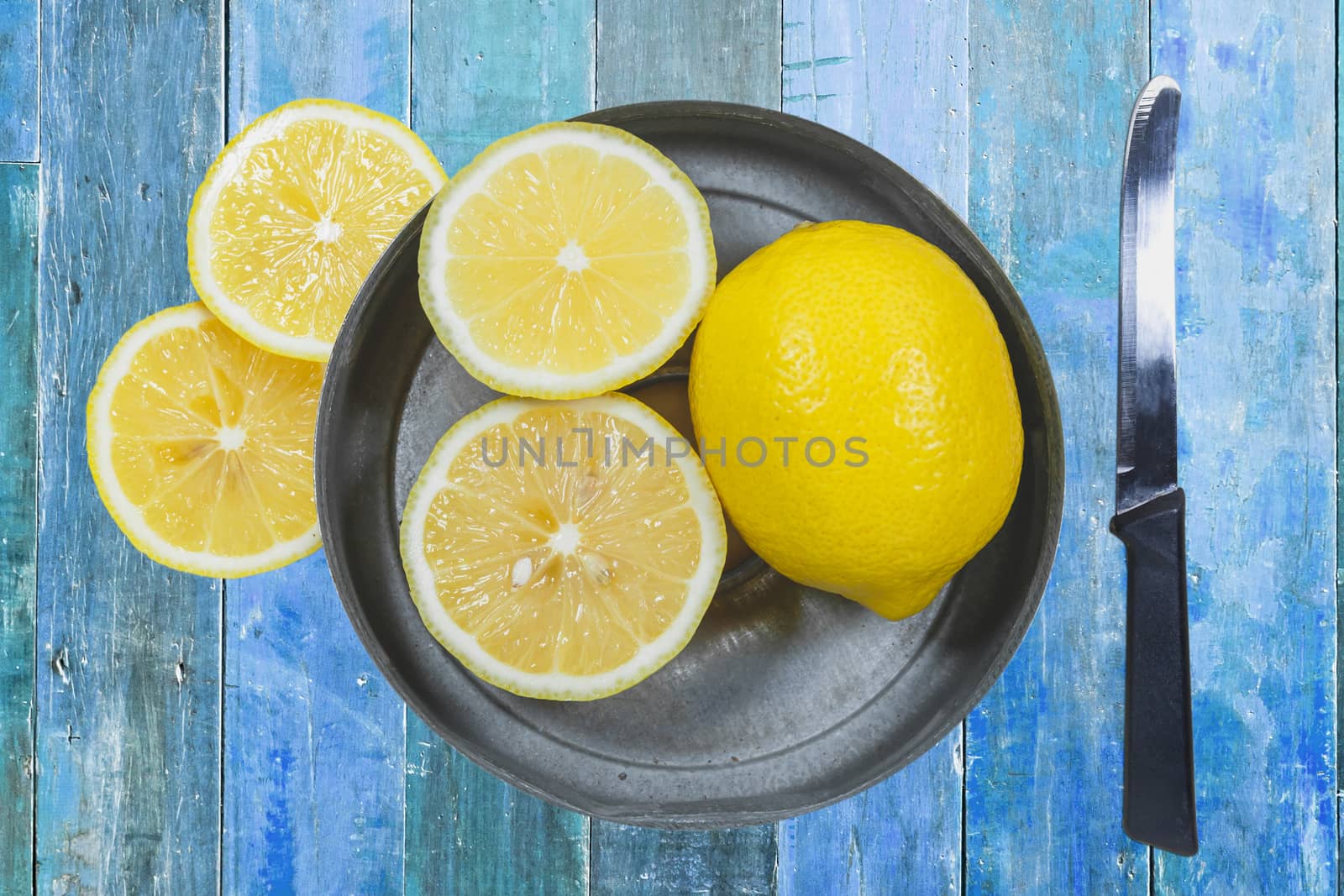 Sliced lemons with knife isolated on blue wood background.