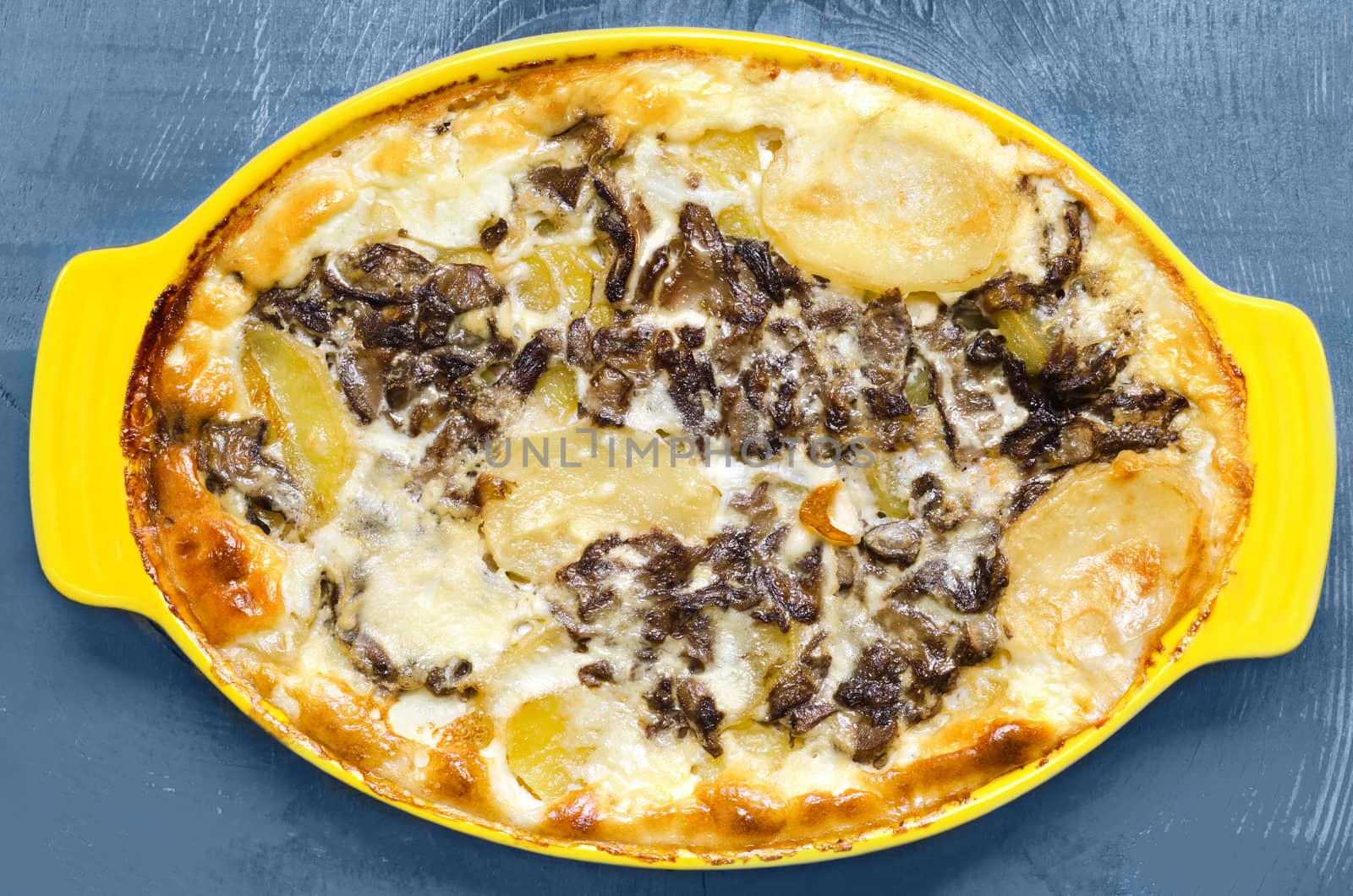 Sliced potatoes with mushrooms, baked in cream, on a blue wooden background