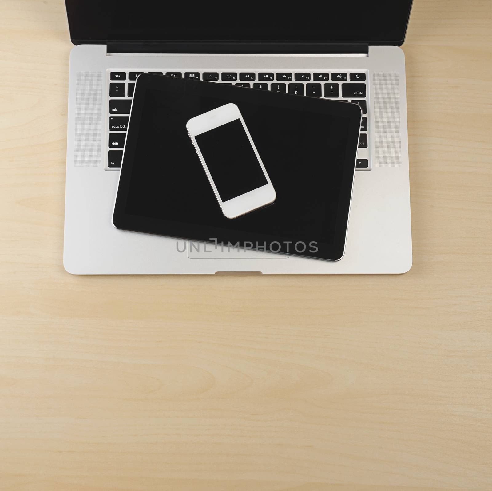 Phone and tablet on top of laptop on wood background