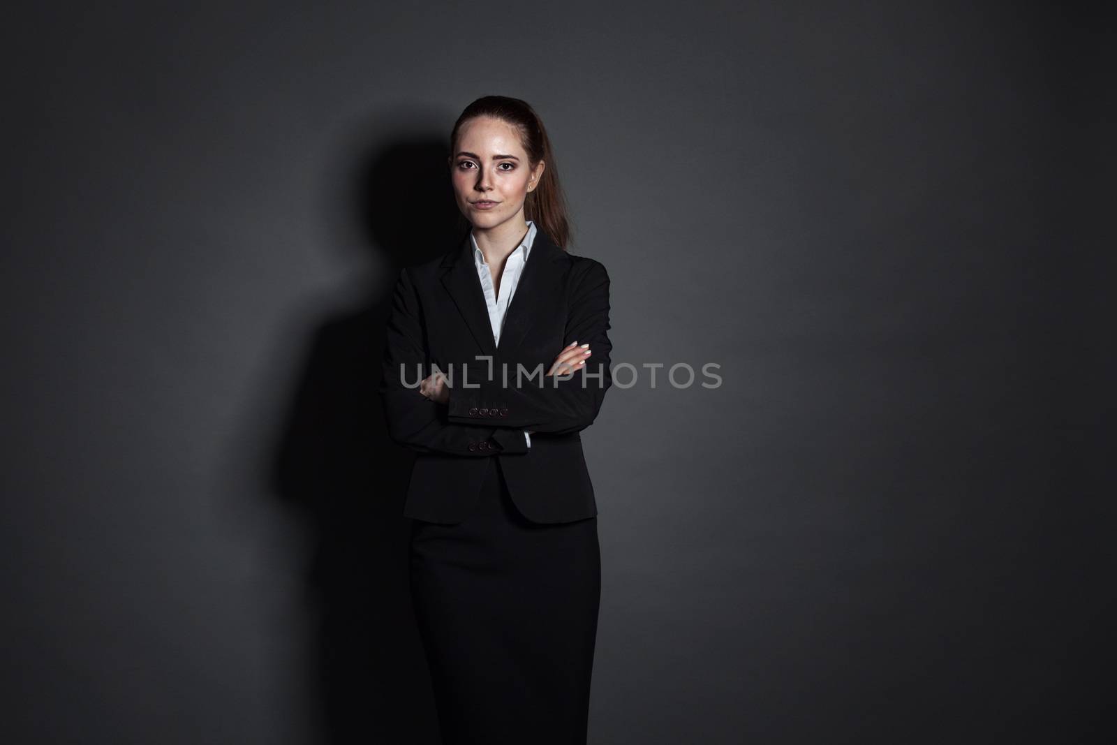 Portrait of young businesswoman in black suit on dark background