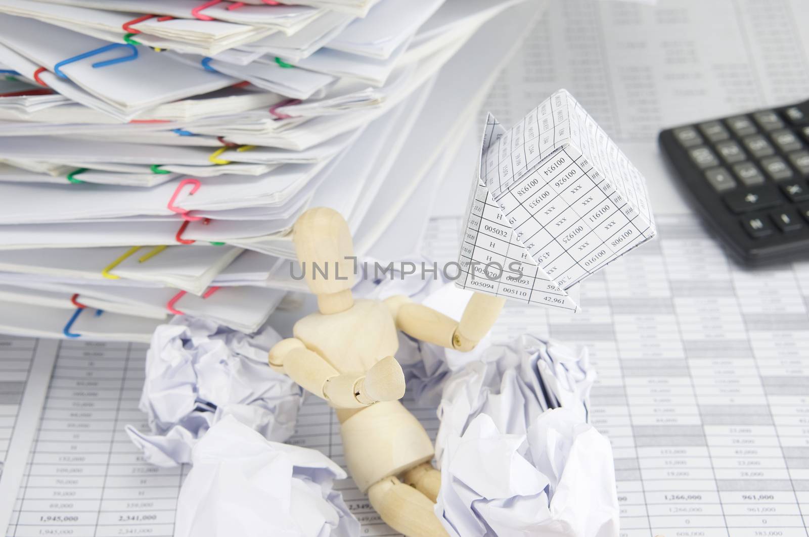 Wooden dummy holding bankruptcy of house with blur paper ball on finance account have overload document of report and receipt with colorful paperclip place confused and calculator as background.