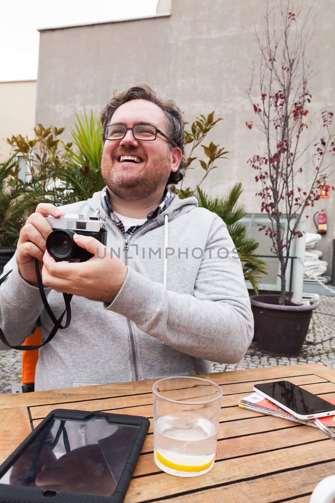 Young traveller man with glasses looking and laughing is having fun with a vintage camera