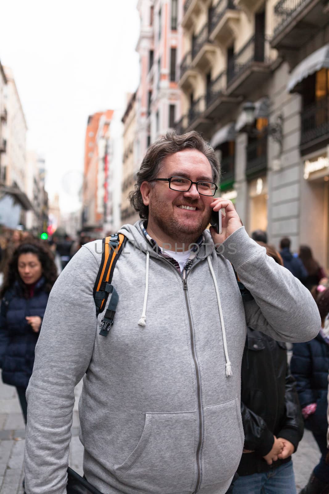 A young man with glasses searching around and laughing and talking by phone