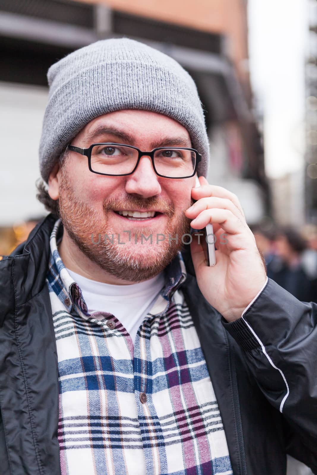 A young man with glasses searching around and laughing and talking by phone