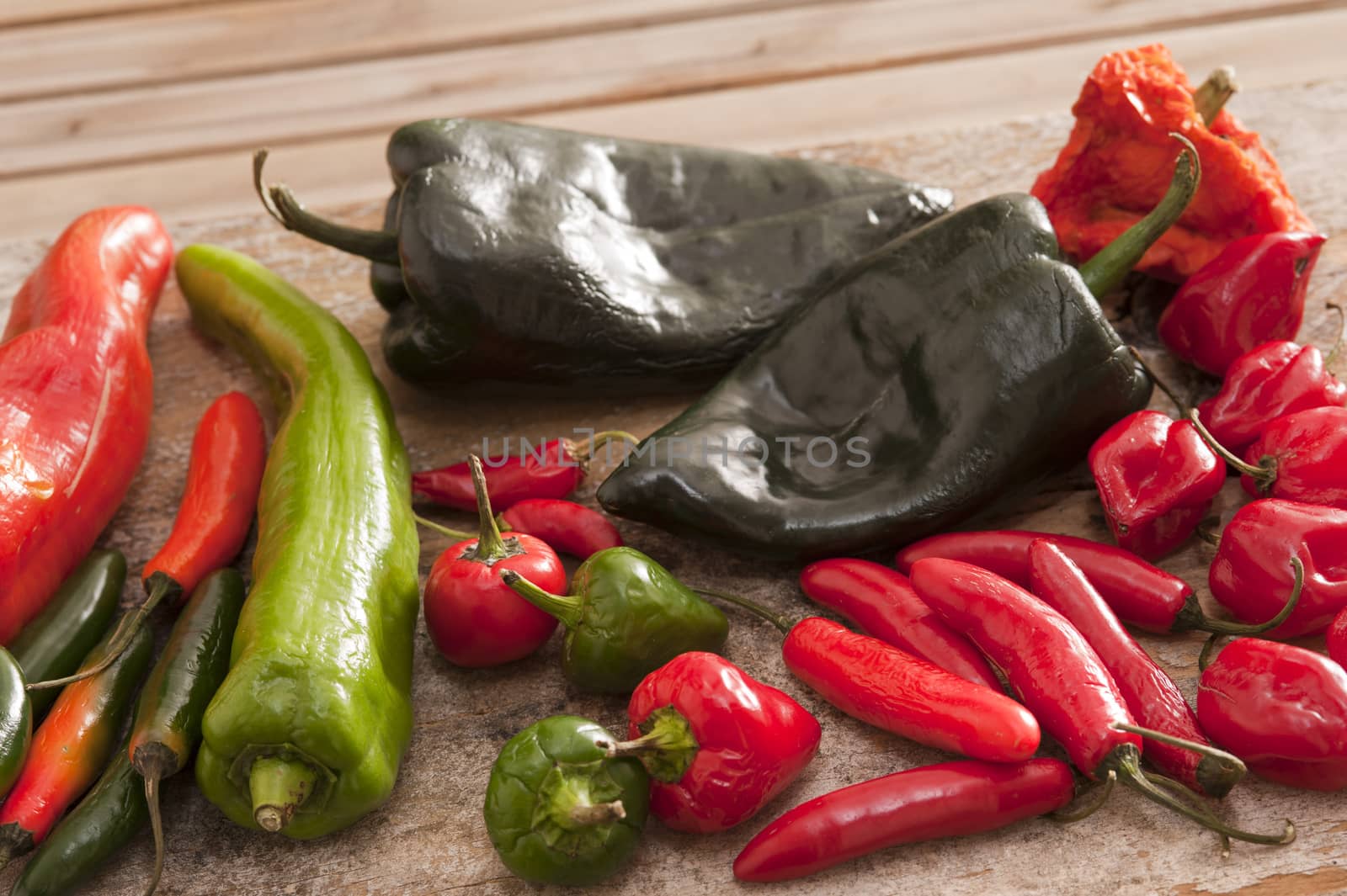 Various long, short, red, green and black hot peppers scattered on cutting board outdoors over wooden table