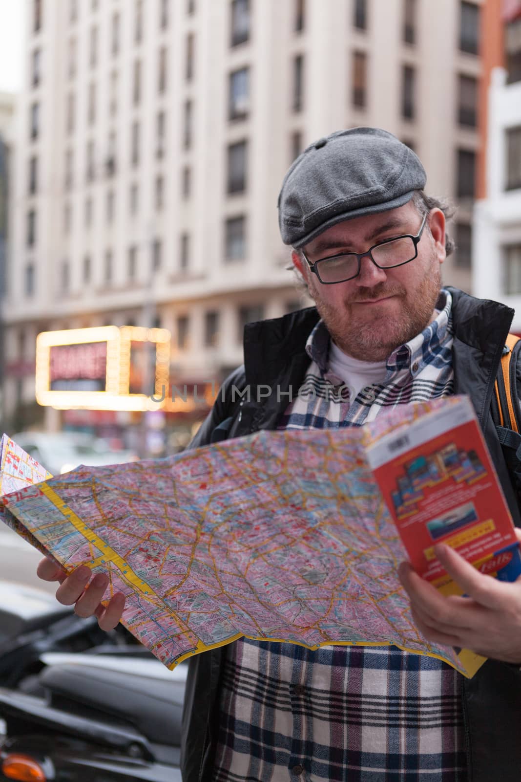 Young traveller man with glasses and a hat  looking for a place in a map looking up