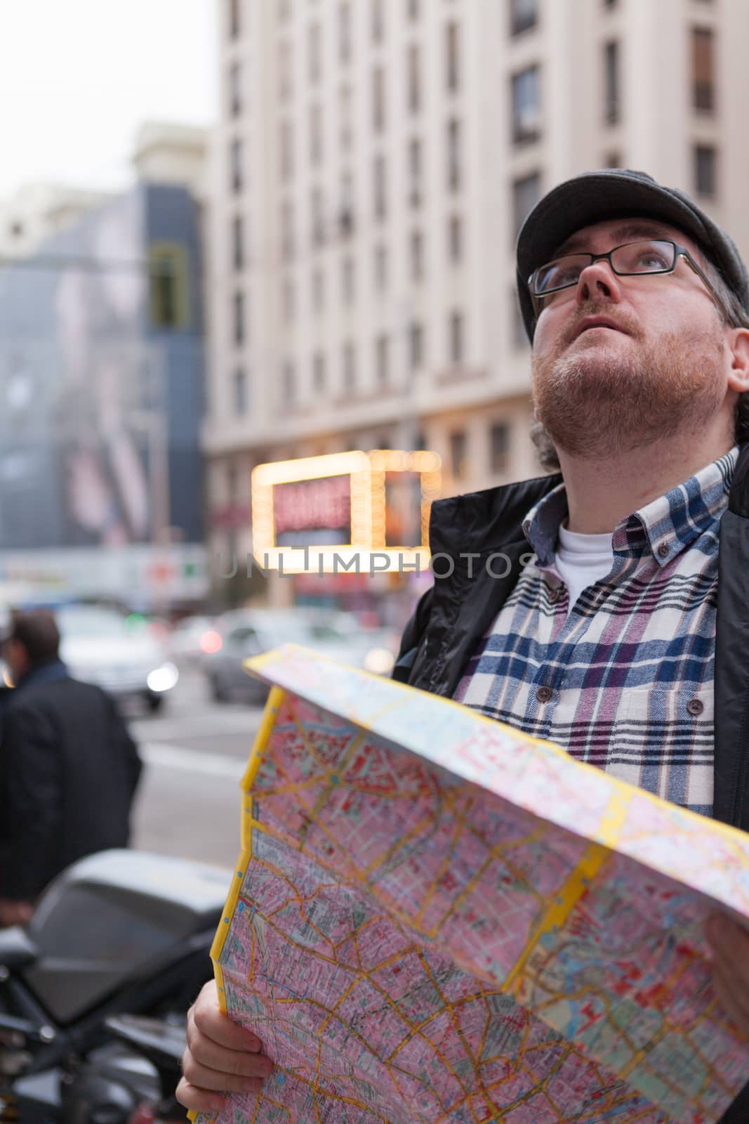 Young traveller man with glasses and a hat  looking for a place in a map looking up