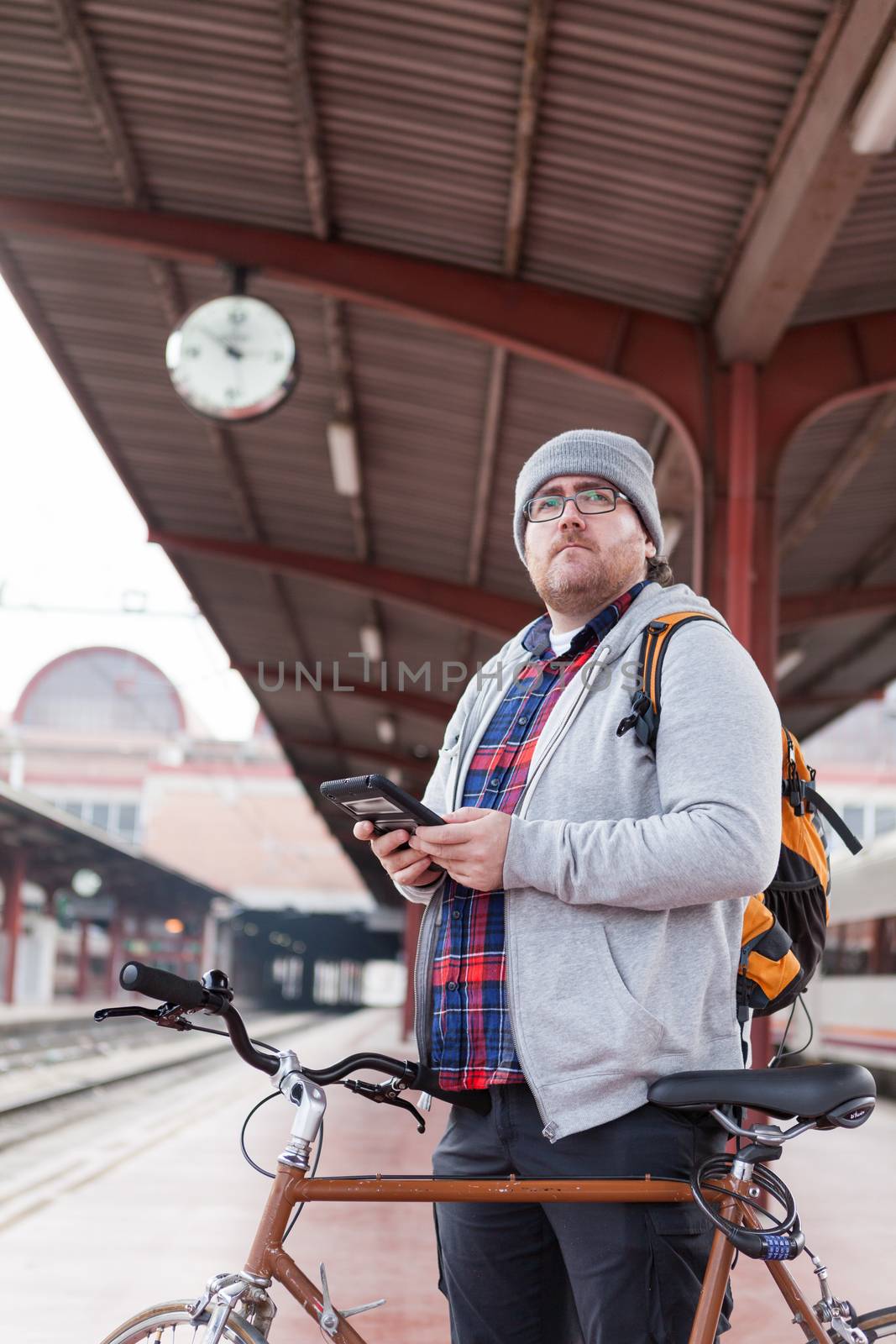 A young man with glasses and a hat is coming into a wagon-train with his bike in a urban scene