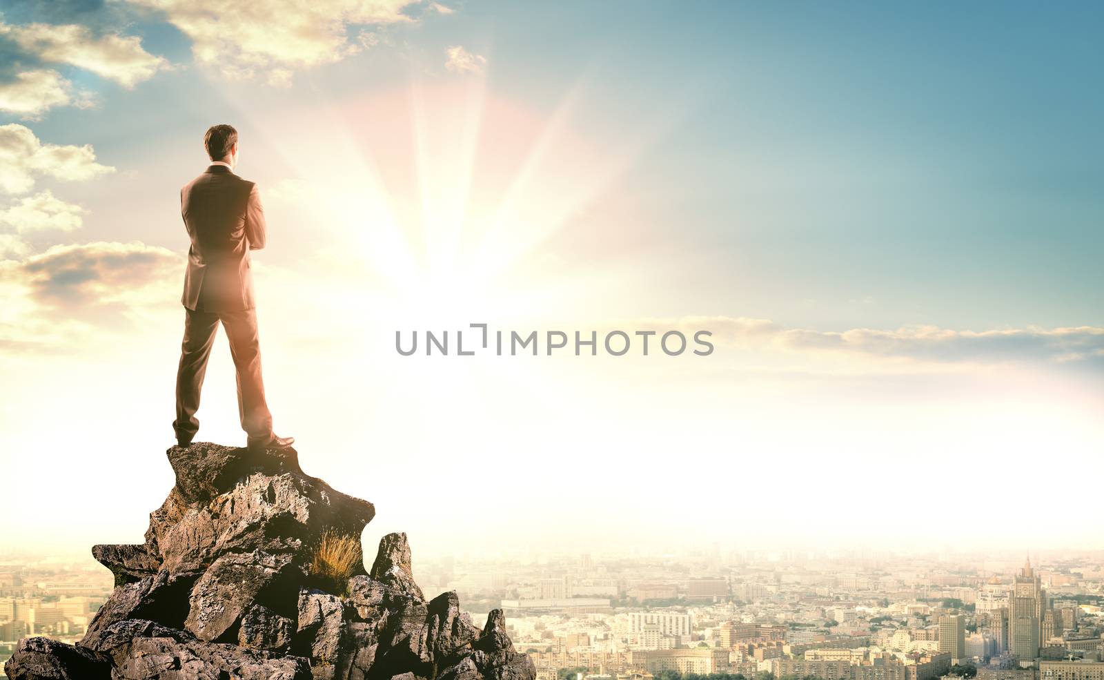 Young businessman standing on edge of rock  by cherezoff