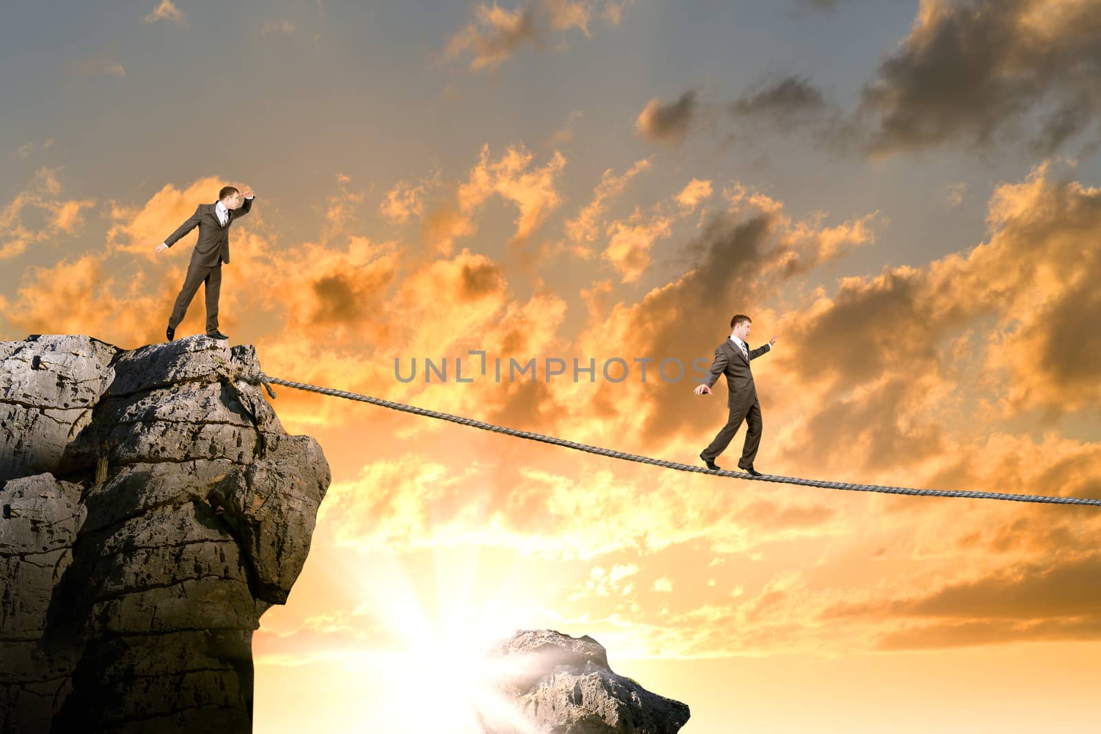 Businessman walking on rope above gap, sunset by cherezoff