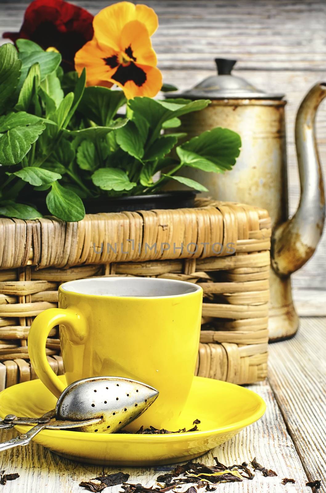 Yellow porcelain cup with tea and basket of decorative Pansy