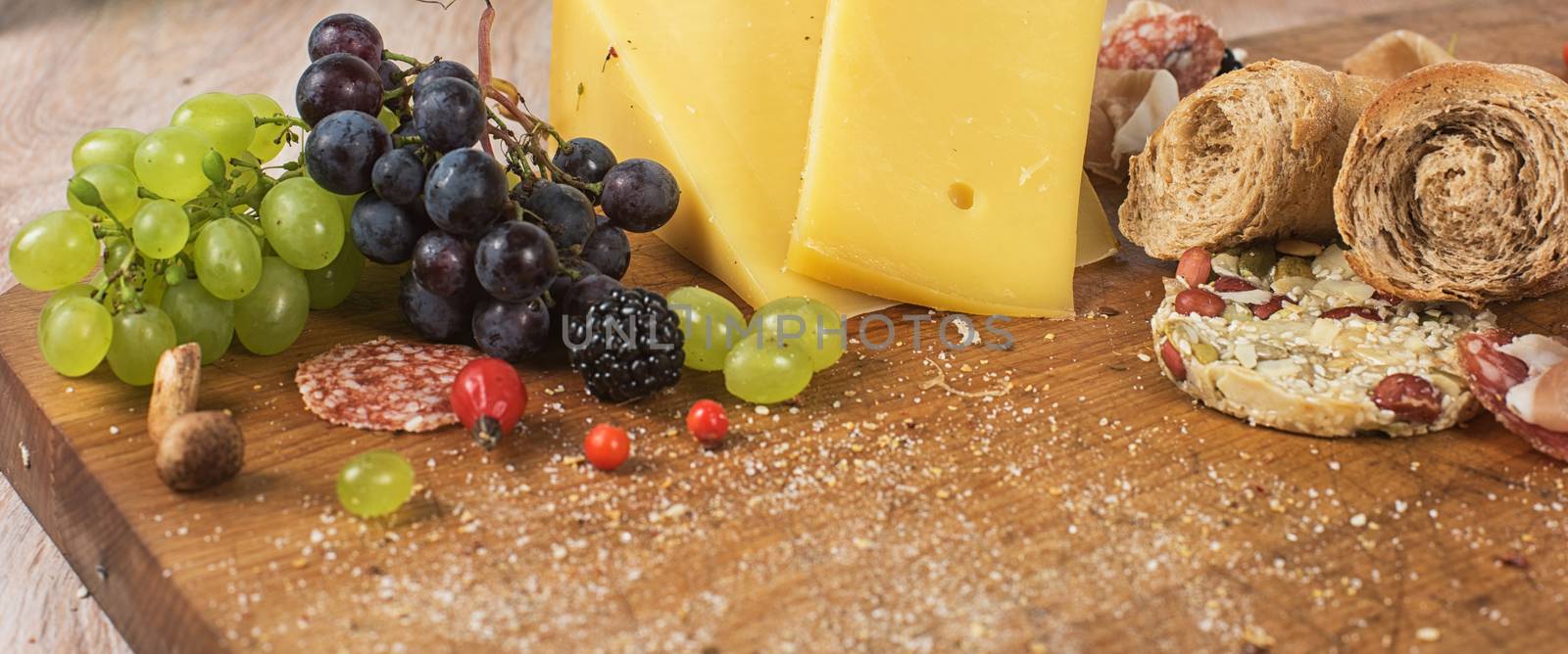 Fresh grapes, cheese bacon berries and salami on wooden table