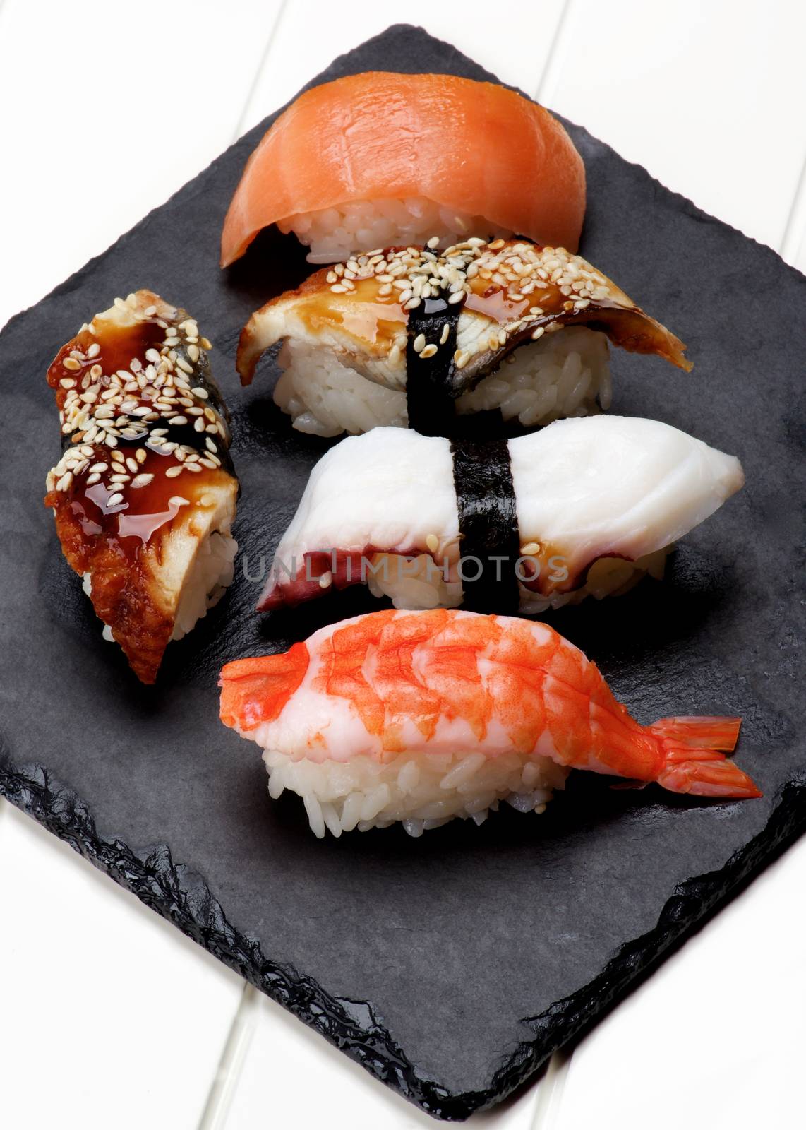 Various Sashimi Sushi with Shrimp, Octopus, Smoked Eel and Salmon on Stone Plate closeup on White Plank background