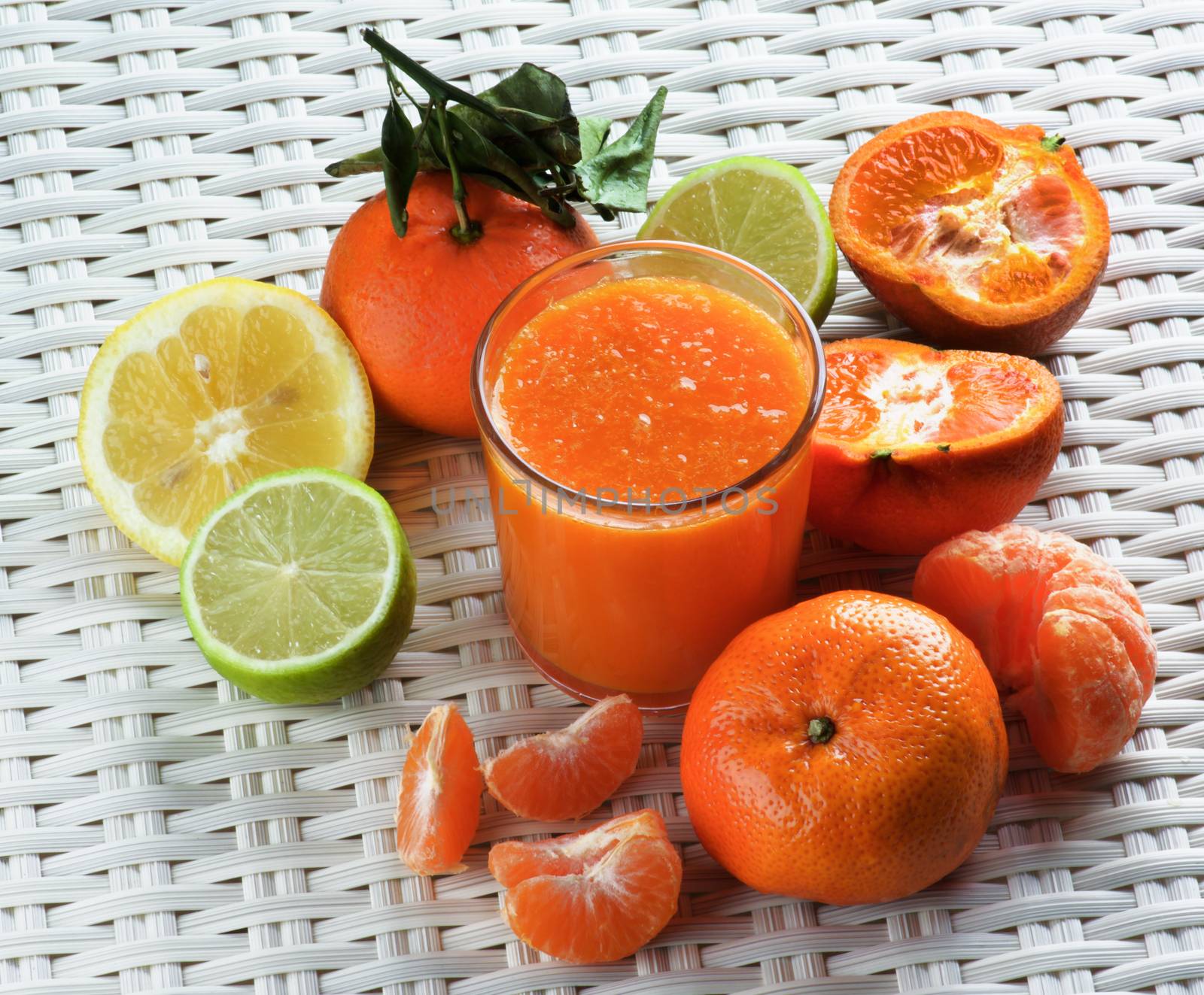 Glass of Freshly Squeezed Mixed Citrus Juice with Tangerines, Limes, Oranges and Lemons closeup on Wicker background