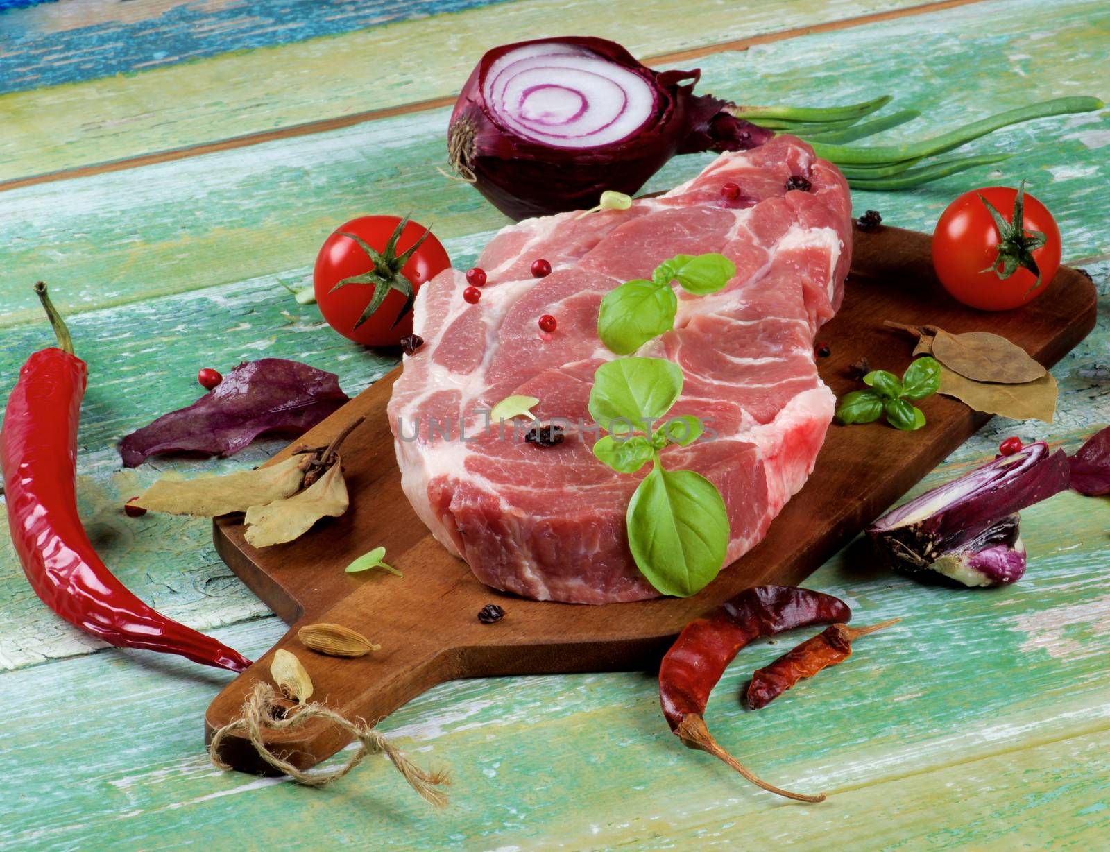 Arrangement of Perfect Raw Pork Neck, Spices, Tomatoes, Red Onion and Fresh Basil Leaves closeup on Cracked Wooden Cutting Board