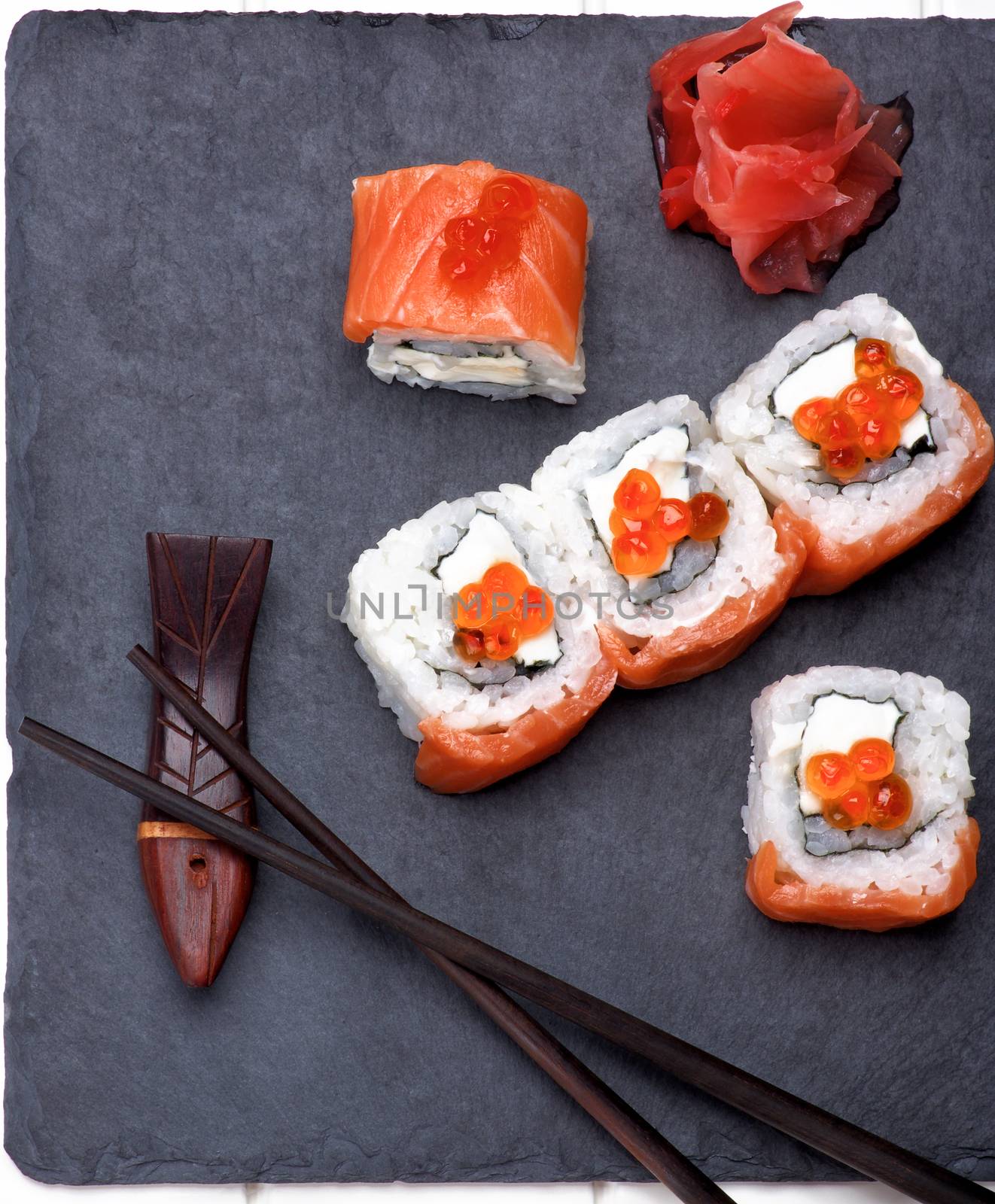 Delicious Sushi with Smoked Sliced Salmon and Gourmet Red Caviar on Stone Plate with Chopsticks and Ginger closeup on White Plank background