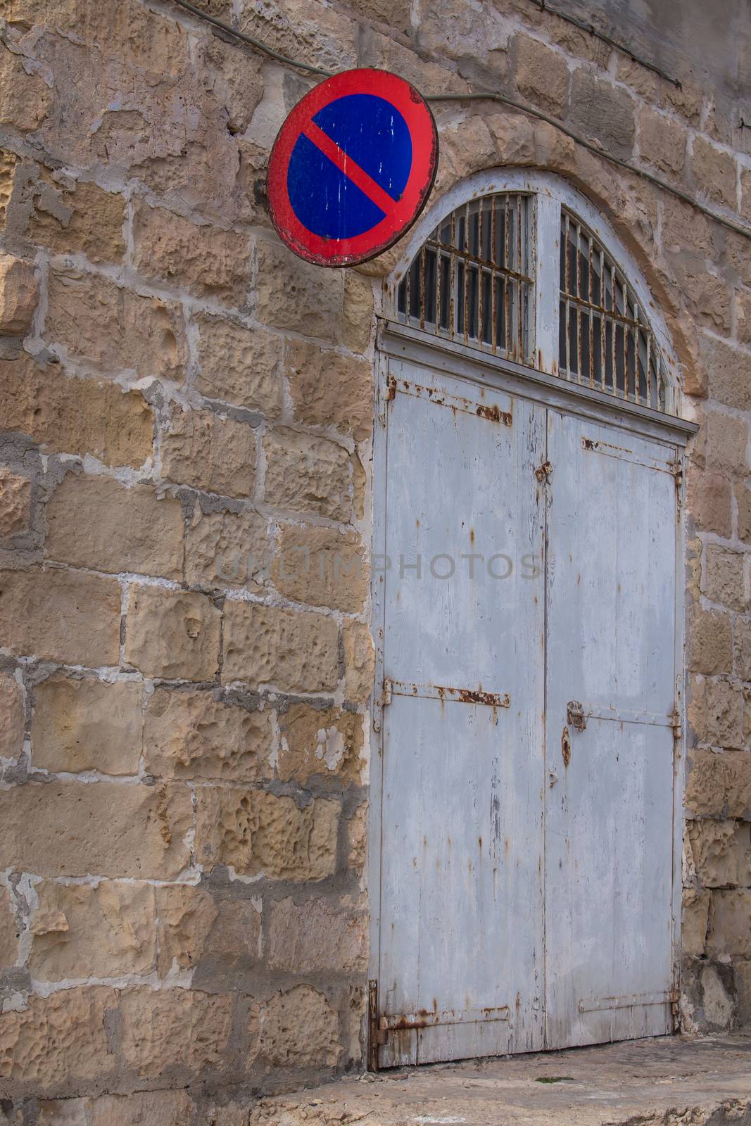 Wall of a building made of stones with a grey old gate and a traffic sign - prohibited parking. Island Malta.