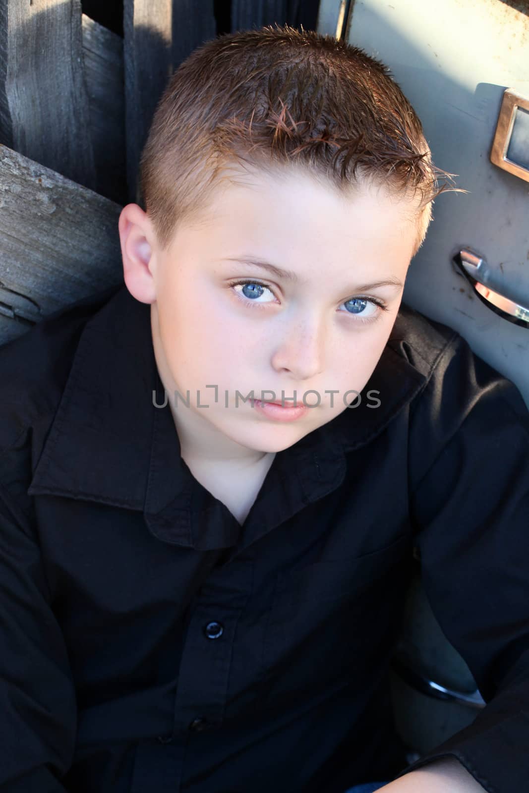 Young boy with deep blue eyes sitting against rustic background