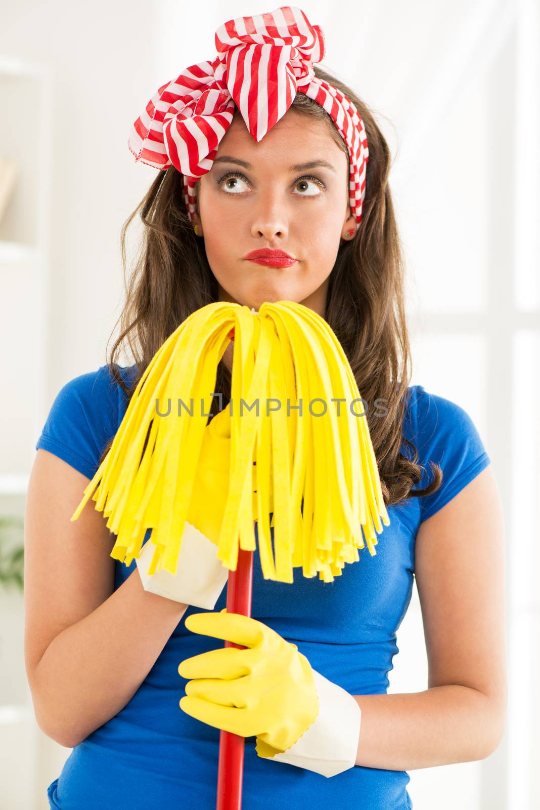 Portrait of a young beautiful unhappy maid holding a mop. 