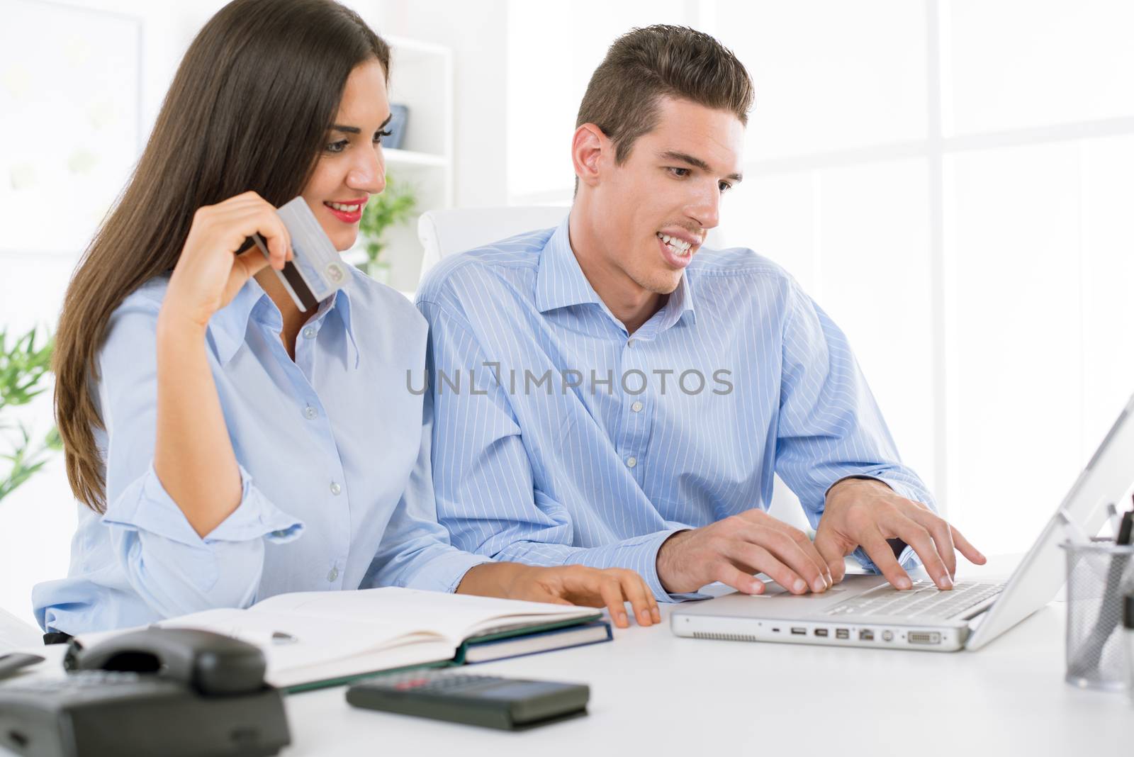 Young beautiful businesswoman and businessman in the office paying something from the internet.