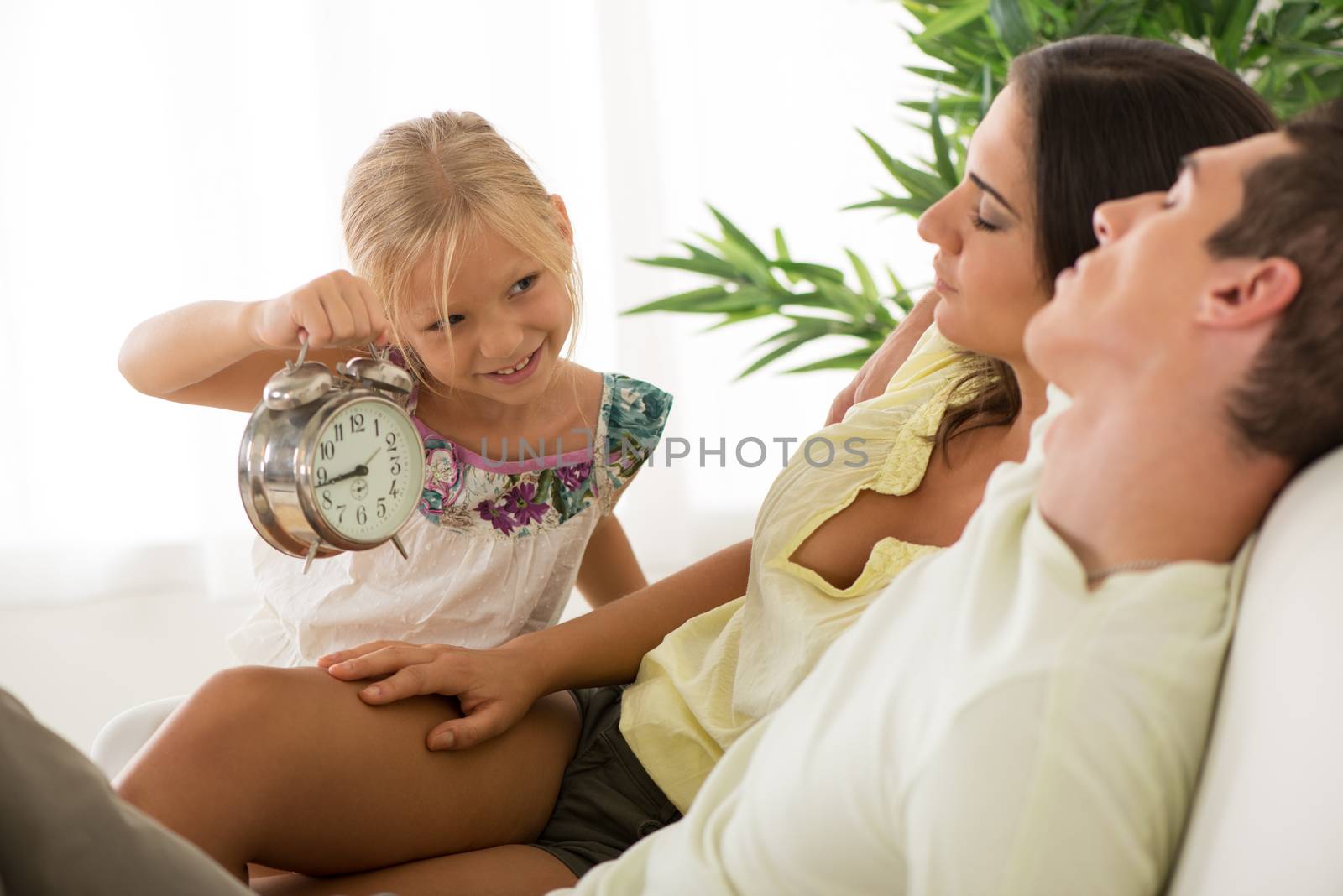 Cute little girl holding an alarm clock and waking up her parents