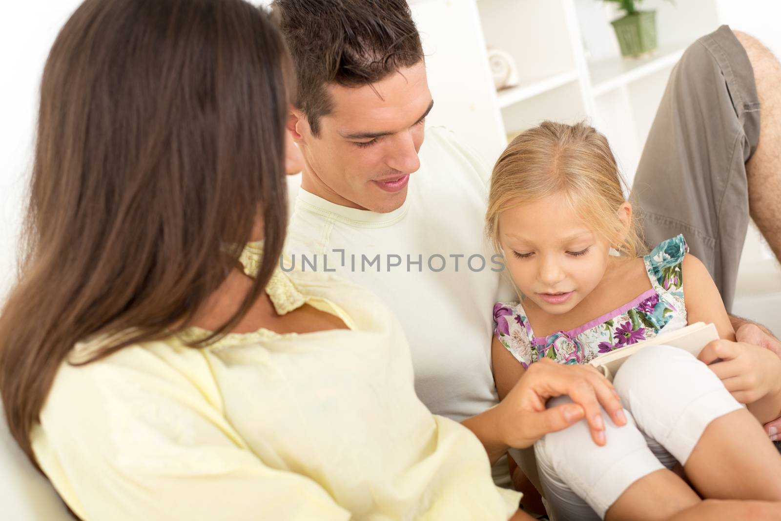 Beautiful Happy young mother and father and their cute daughter sitting at home and reading book