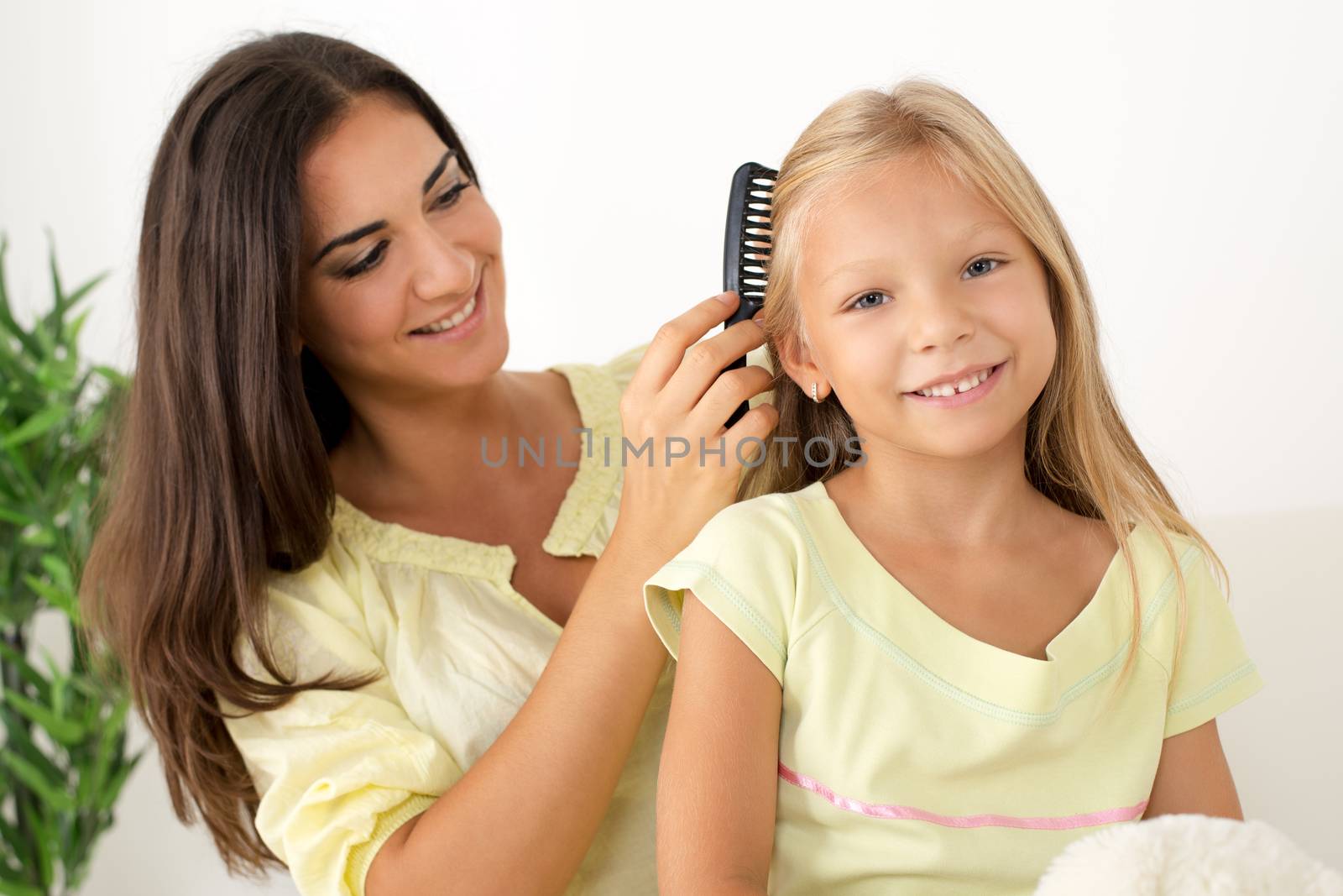 Beautiful young Mother combing her cute daughter at home. 