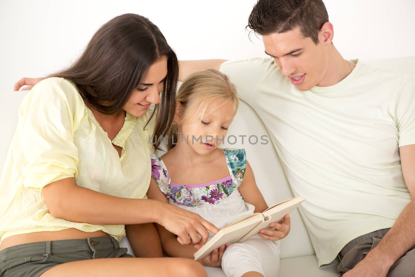 Beautiful Happy young mother and father and their cute daughter sitting at home and reading book