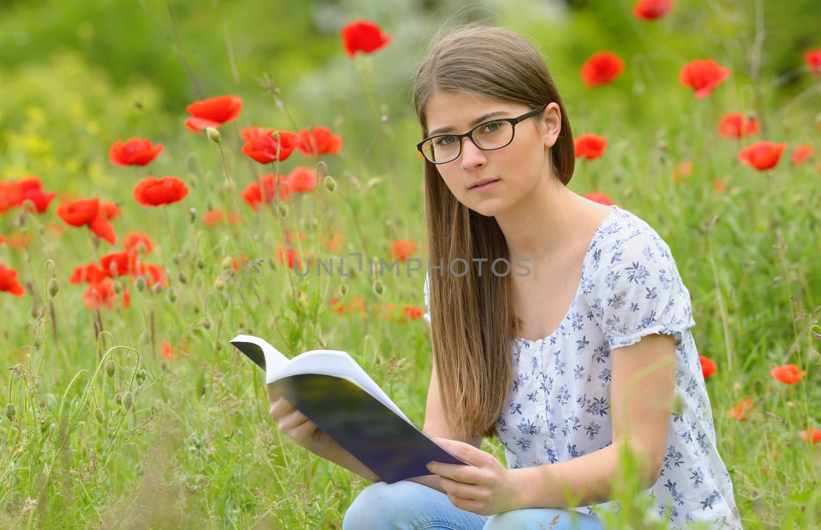 Teen girl reading book in the poppies field