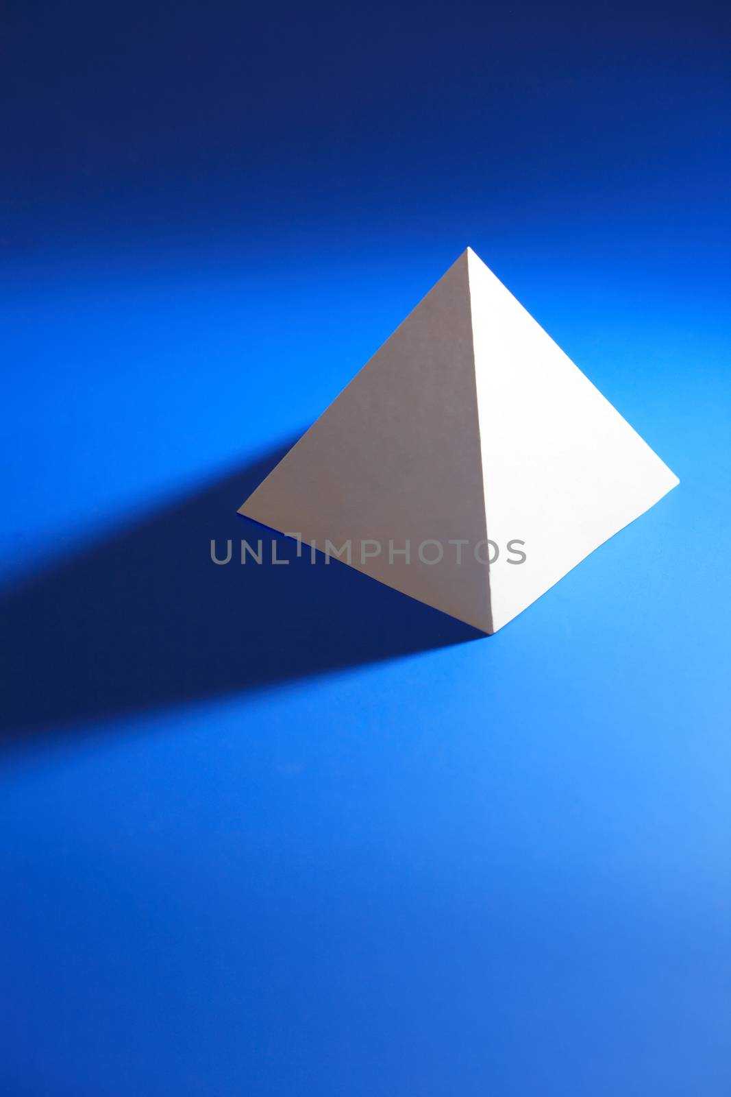 Geometry concept. One white paper pyramid on blue background