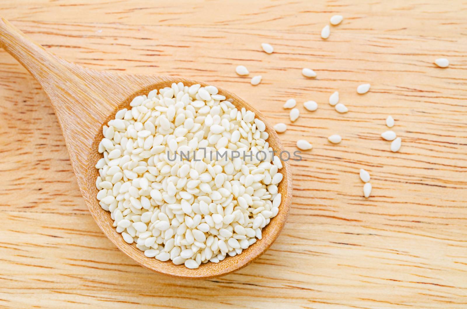 White sesame seeds in wooden spoon on wood table.