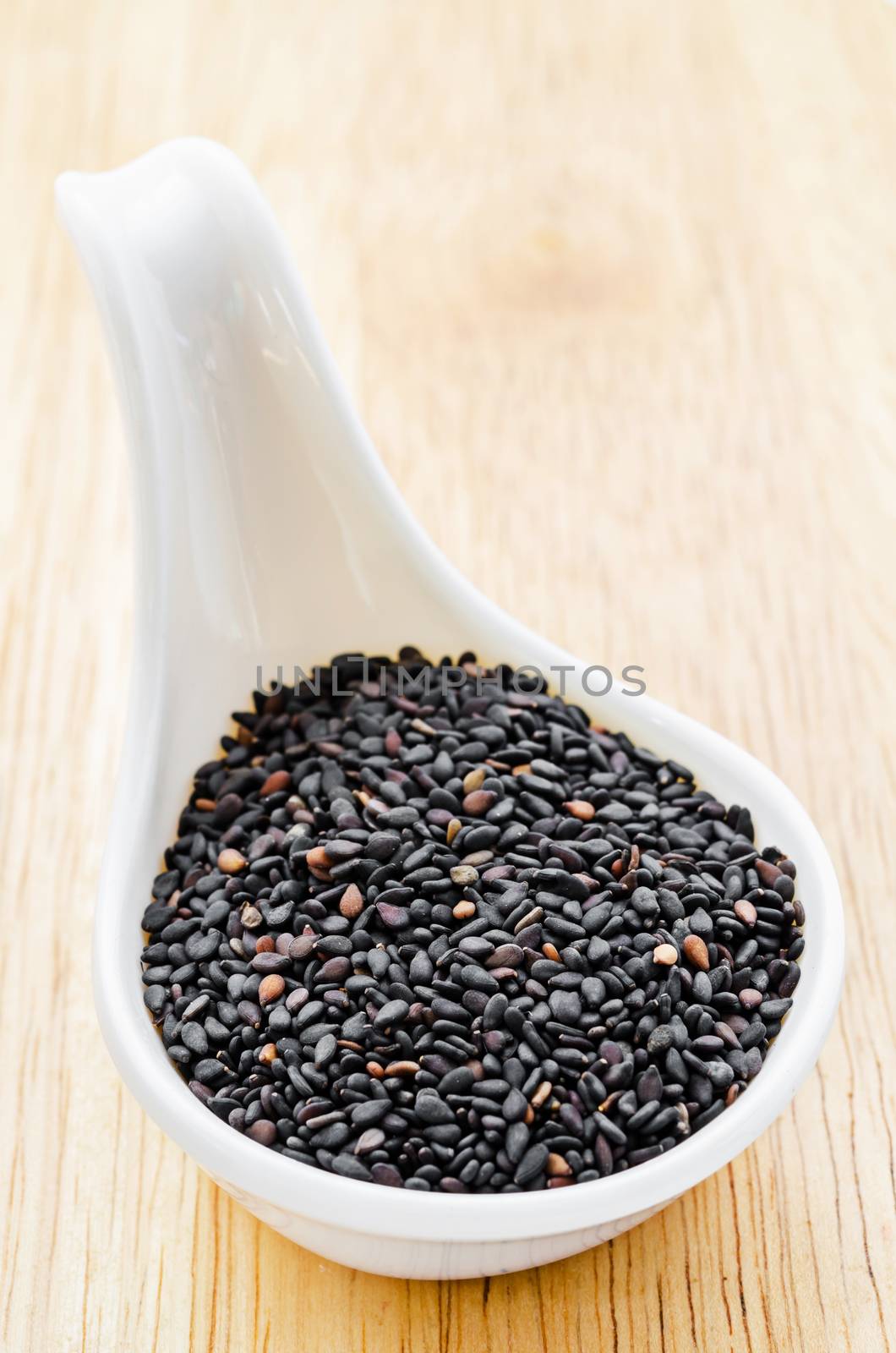 Black sesame seeds in white spoon on wood table.