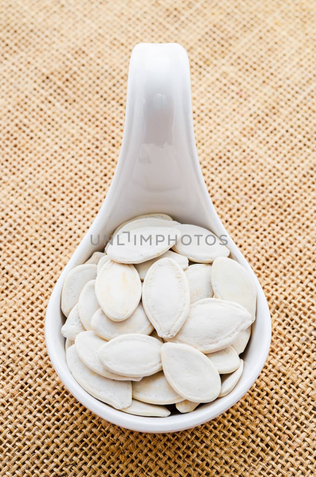 Pumpkin seeds in a white spoon on sack background.