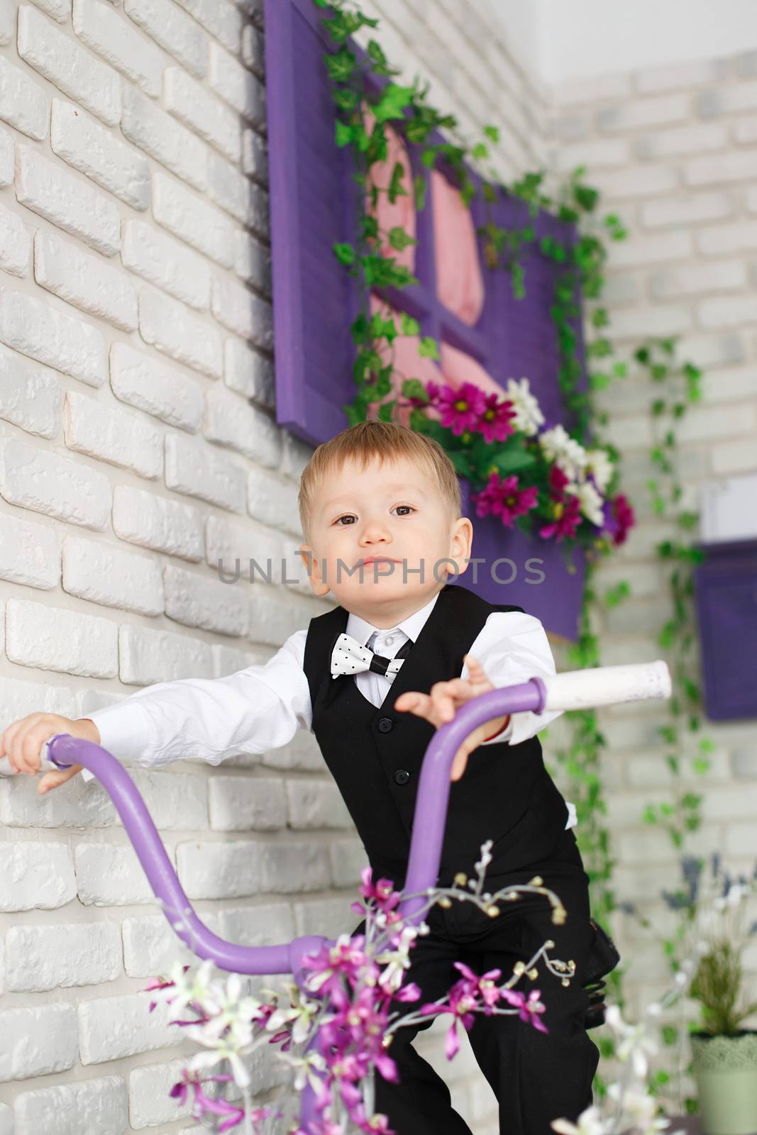 Portrait of an elegant little boy on a bicycle in studio decorated