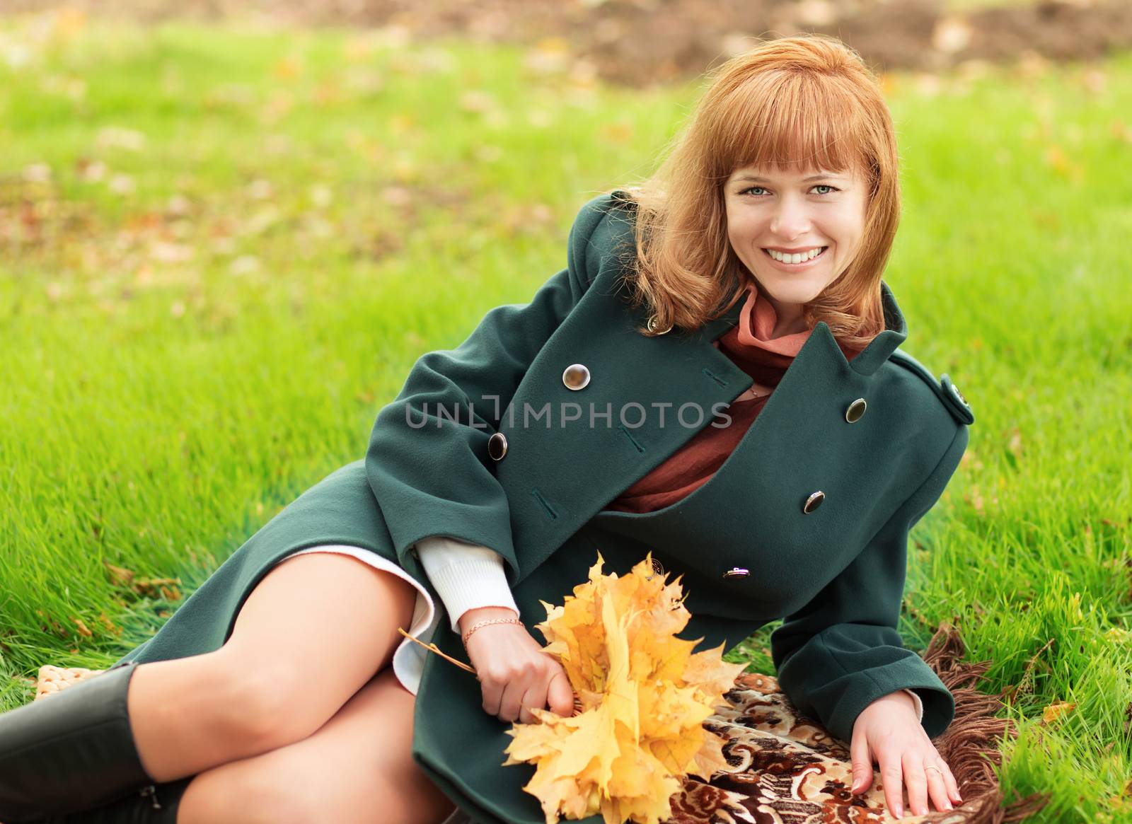 Portrait of happy smiling woman lying on the grass in autumn park with a bunch of leaves