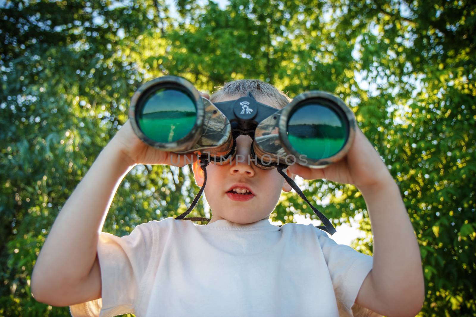 Little boy looking through binoculars on river bank