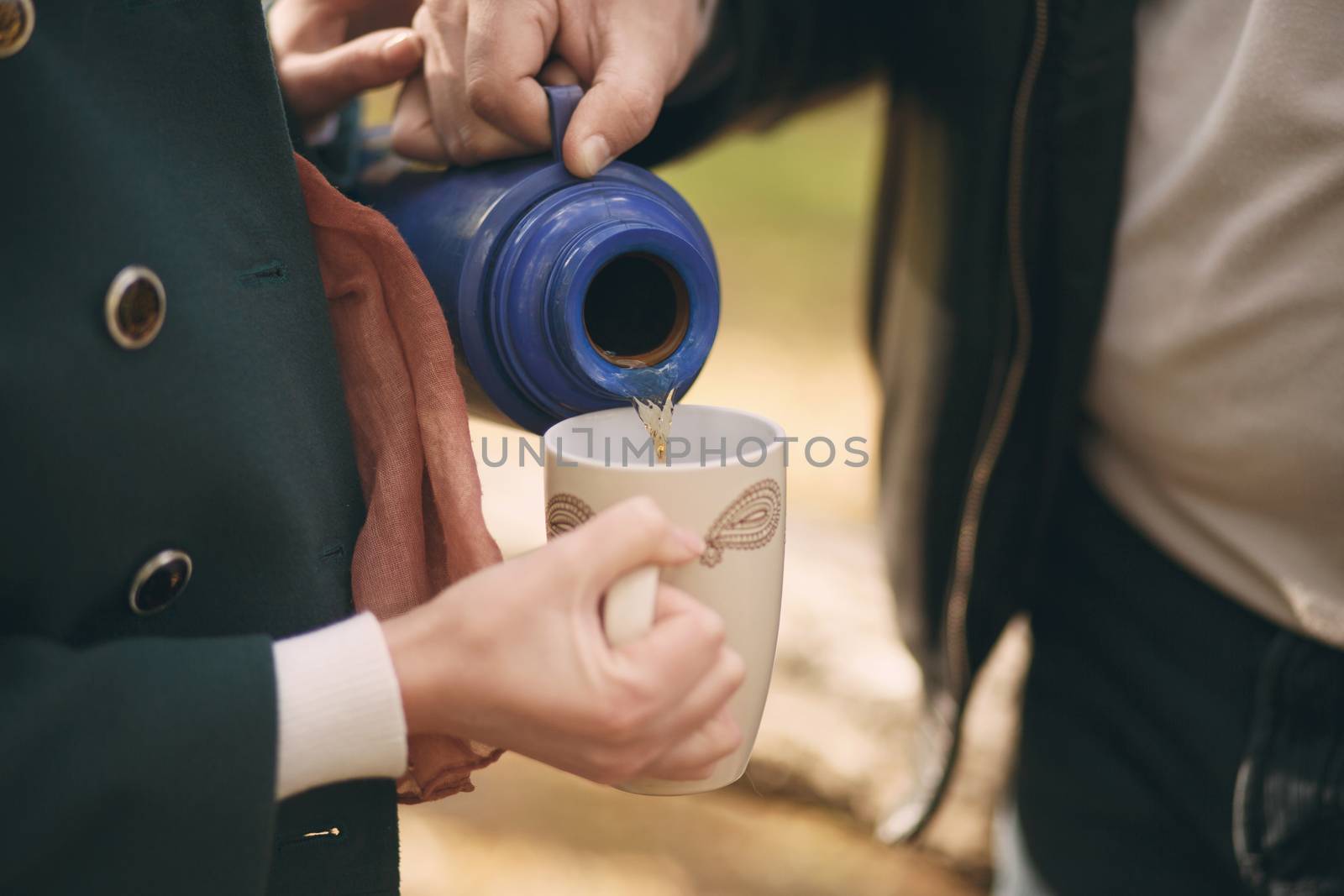 Couple in love pours tea from a thermos into the cup to warm up on the street