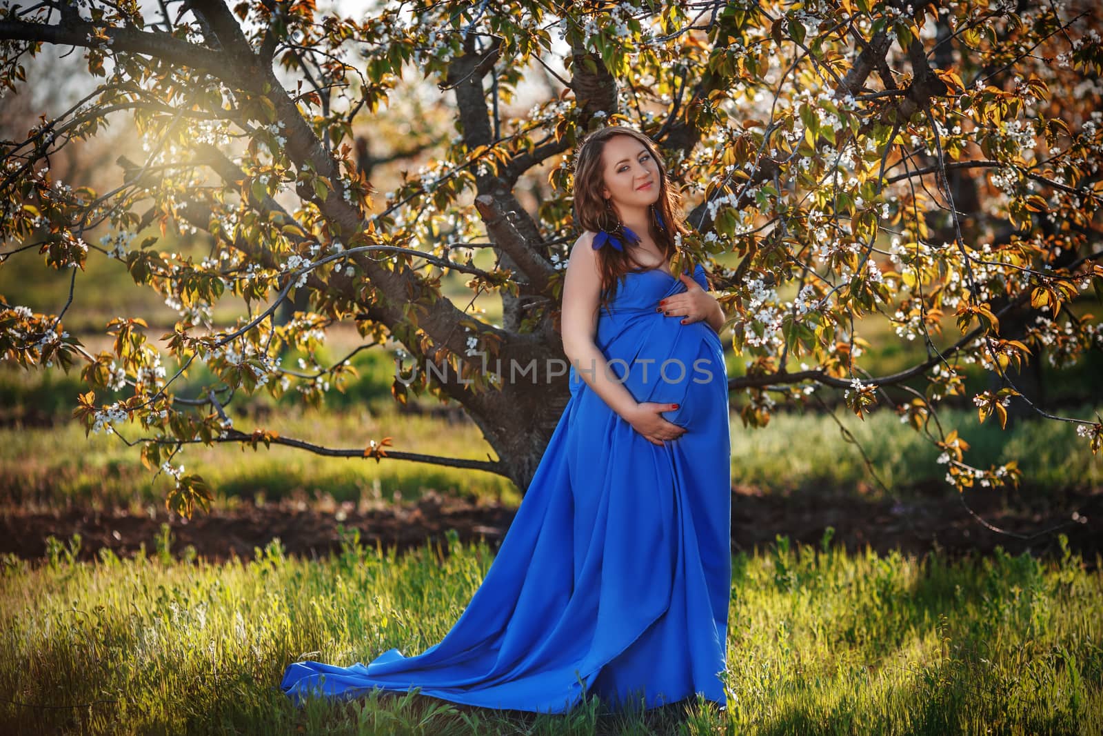 Beautiful pregnant woman in the lush spring garden in full growth