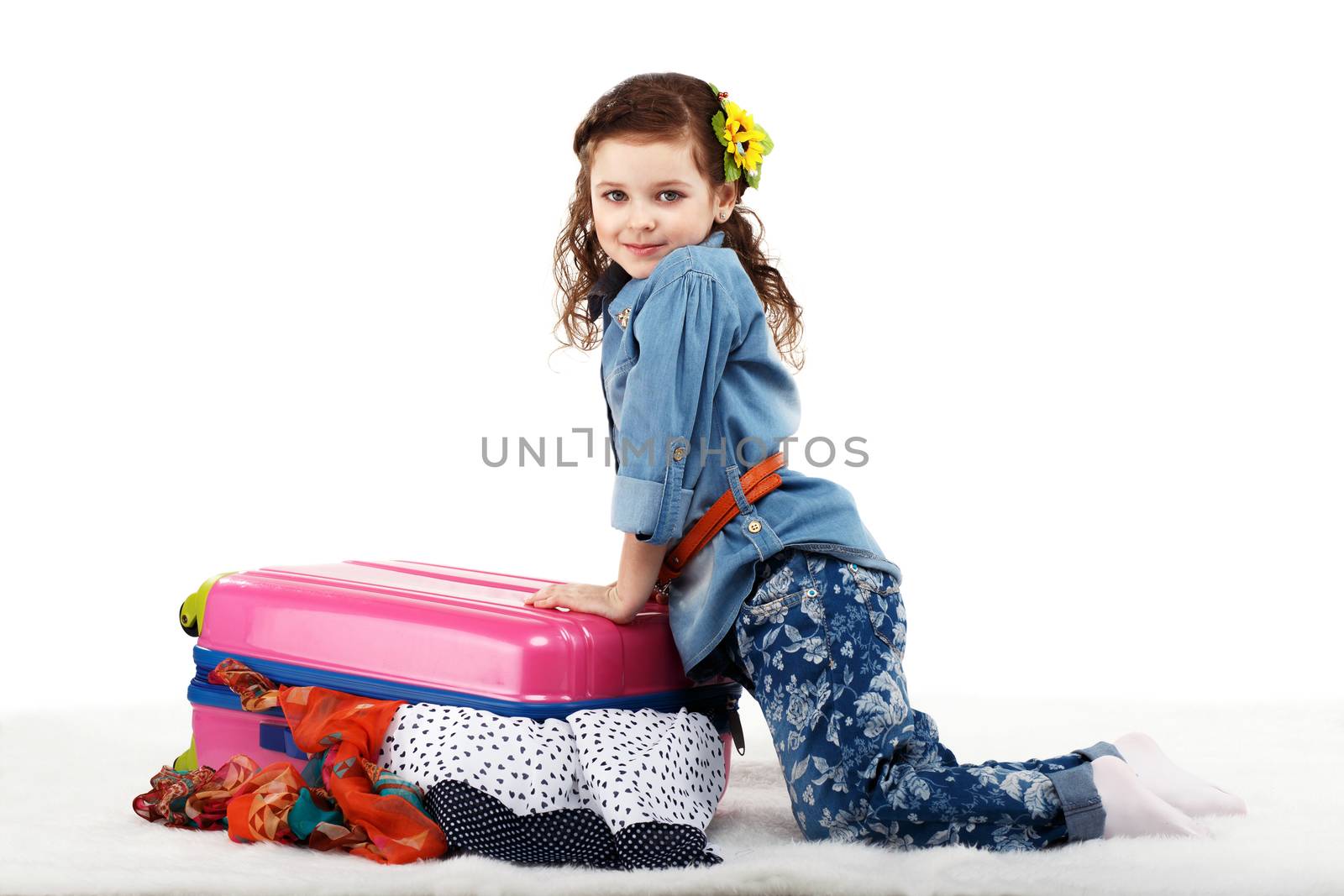 Fashionable little girl closes the suitcase with clothes isolated on white background