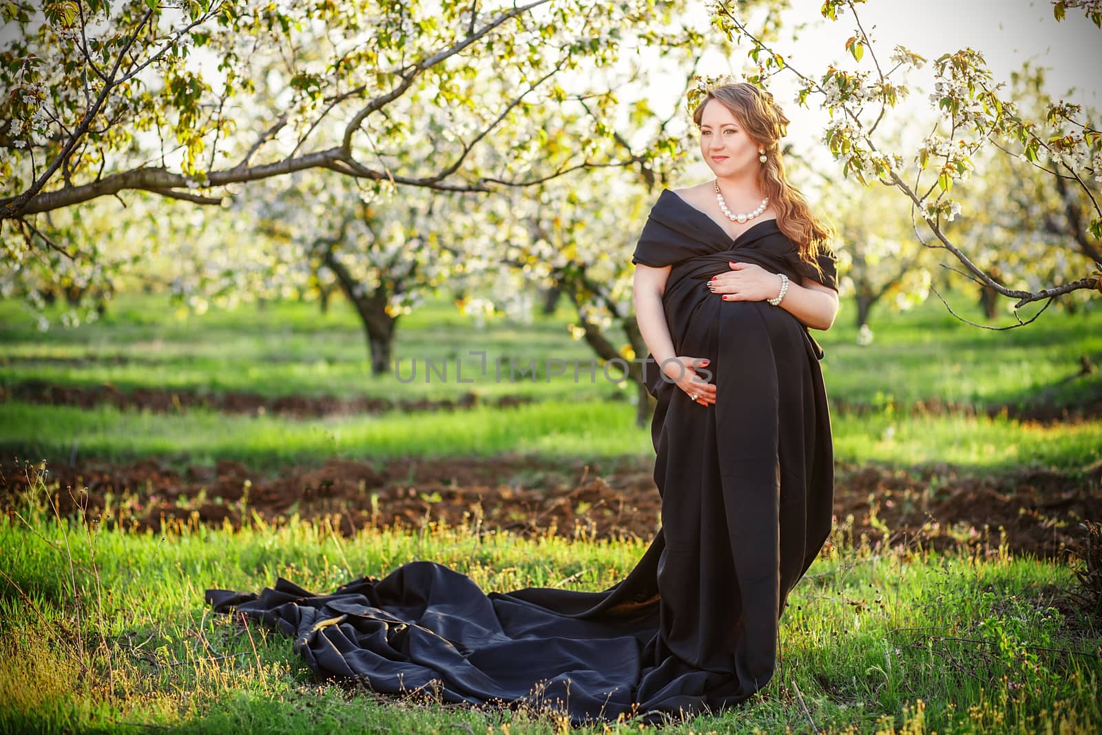 Beautiful pregnant woman in black in the lush spring garden in full growth