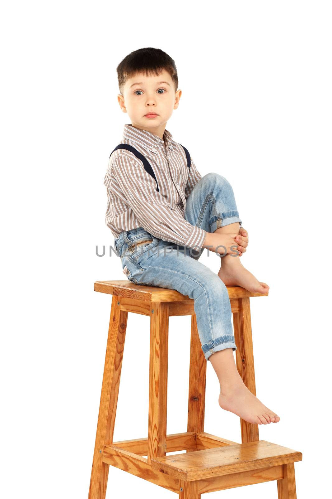 Portrait of a funny little boy sitting barefoot on a high stool isolated on white background