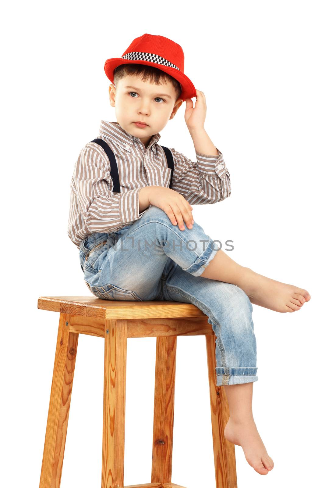 Portrait of a funny little boy sitting on a high stool in a red hat isolated on white background