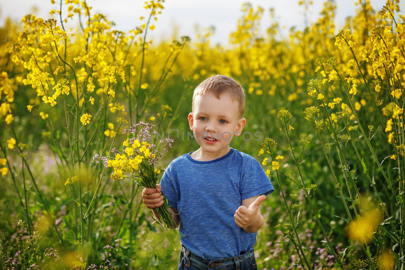 Little happy boy with a bouquet of flowers is in the yellow flowering rapeseed field