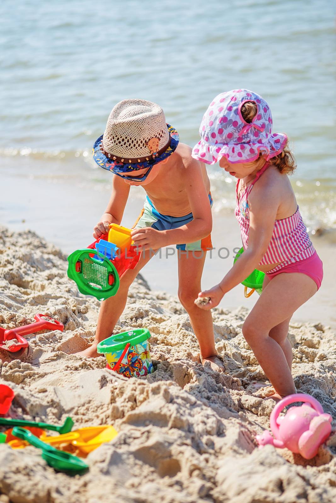 little girl and boy playing on the beach by natazhekova