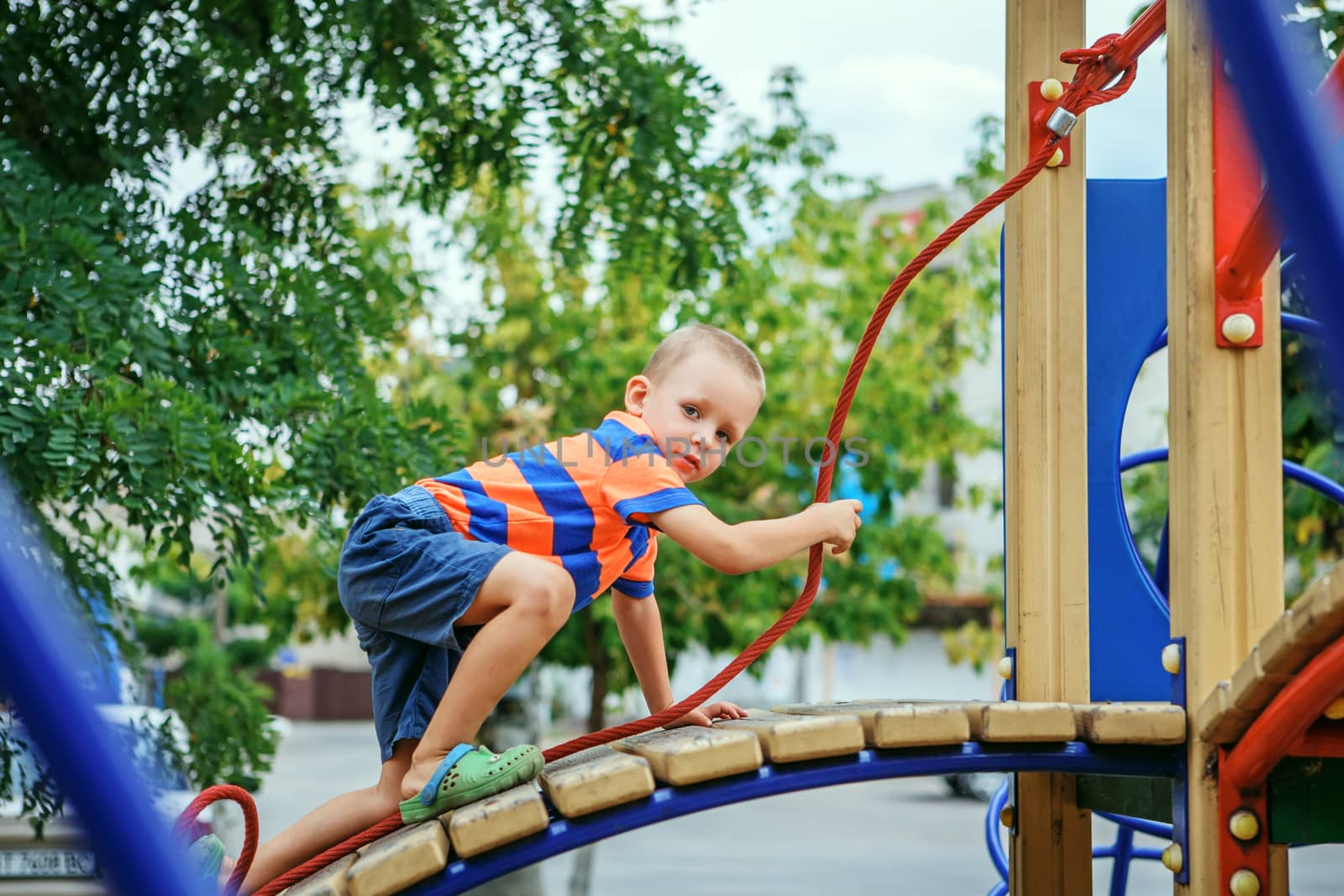 Cute little boy playing on the playground in the summer by natazhekova