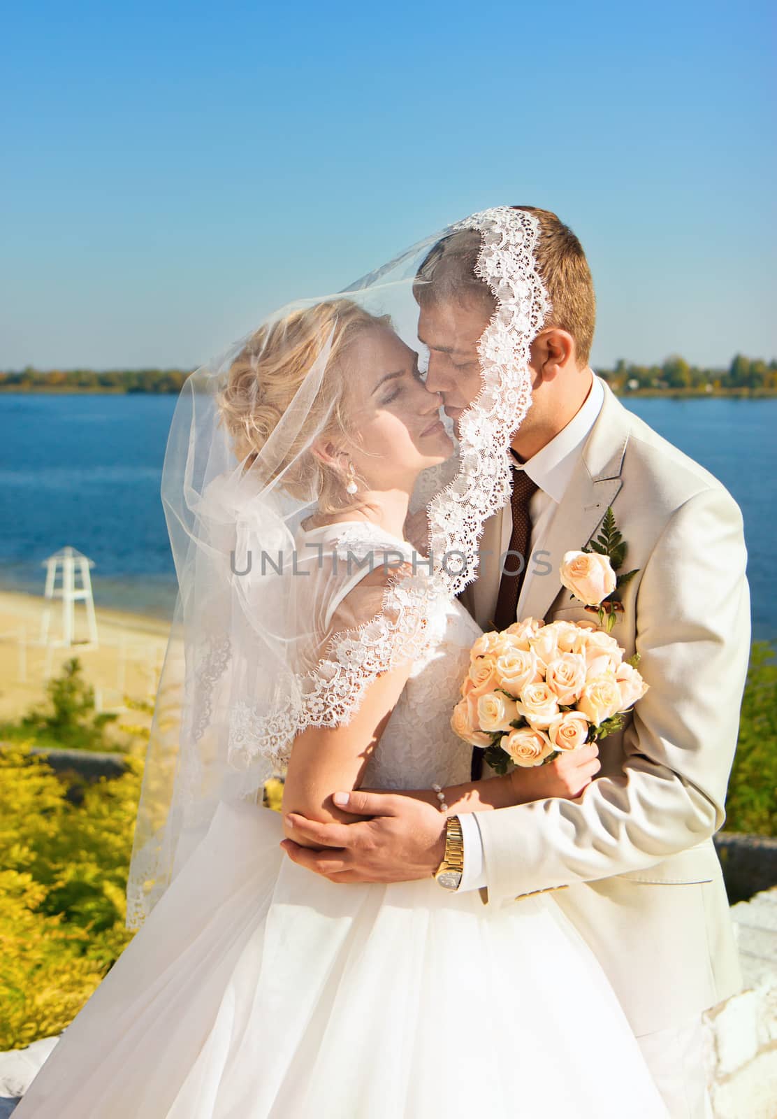 Loving bride and groom sheltered veil bride embrace on the river bank