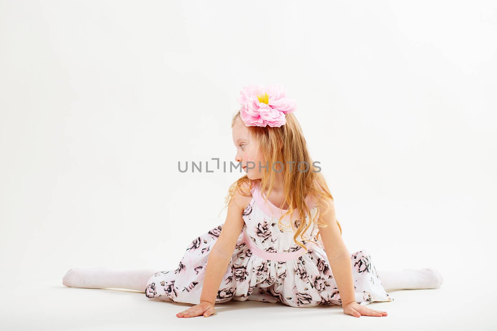 Little blond girl in a dress sitting on the twine against a white background. facial profile