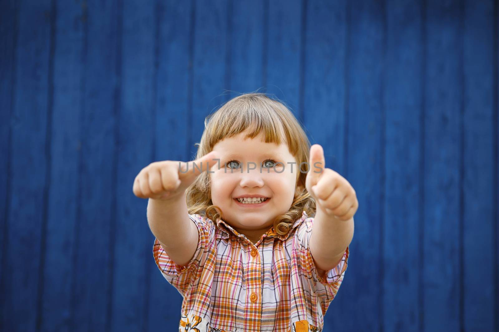 Portrait of happy joyful beautiful little girl against the old textured blue wall gesturing thumb