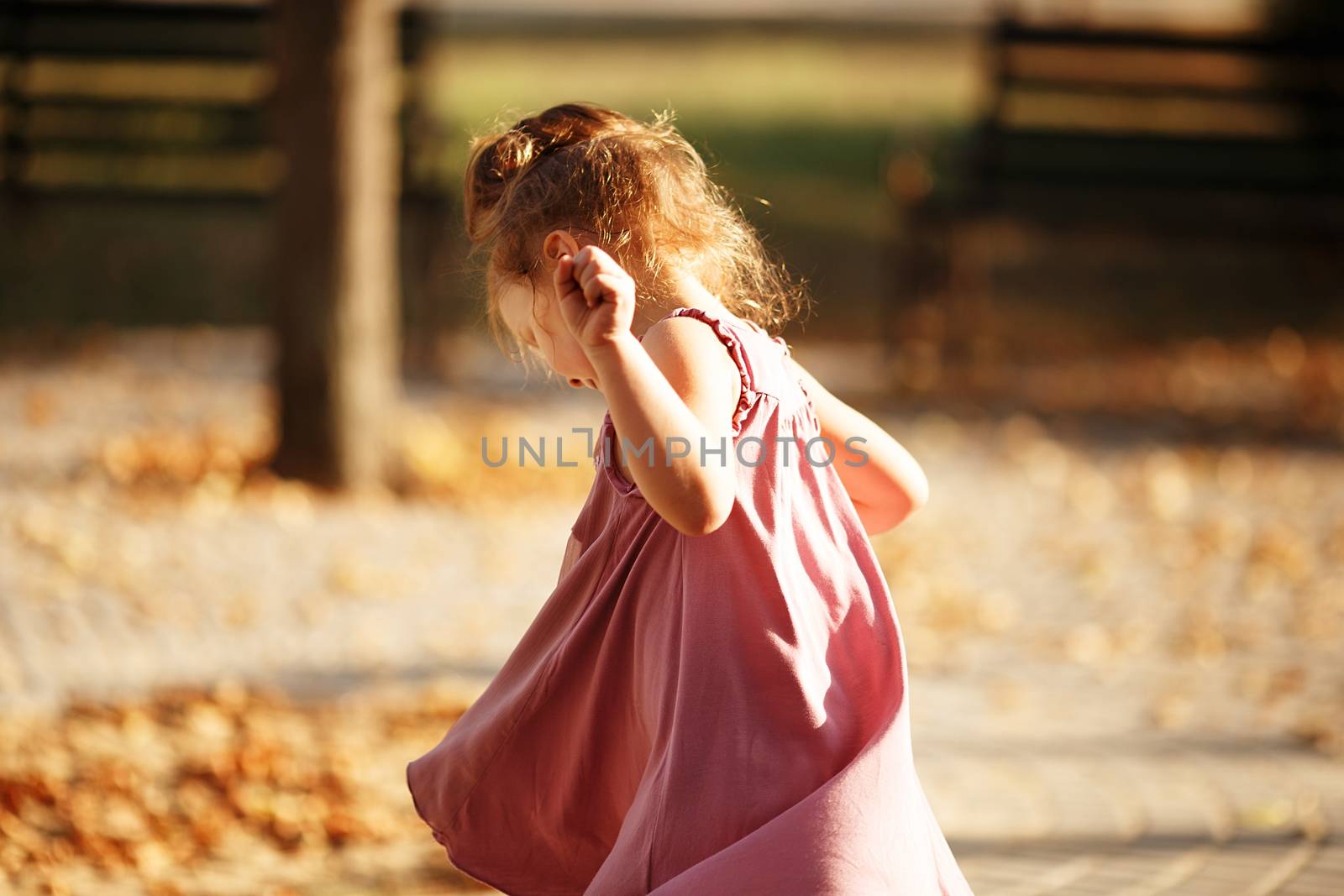 Portrait of a little girl dancing in the park a warm autumn evening. In move. Back view