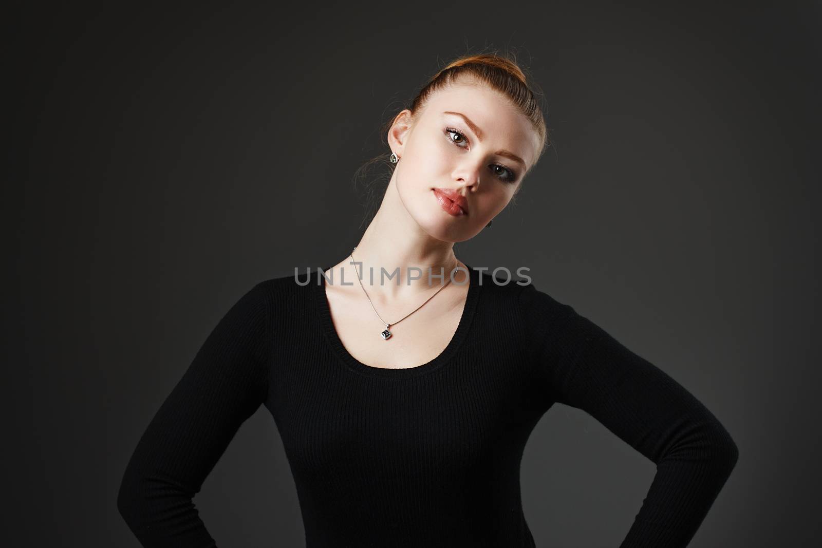 Portrait of a young beautiful girl in black on a gray background in the studio. Woman dancer or ballerina.